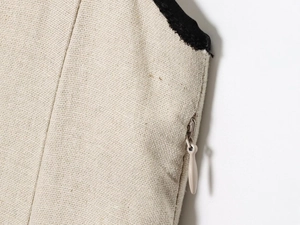 Detailed macro view of invisible zipper on cream linen dress with black contrast trim