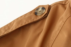 Detailed close-up of double-stitched twill fabric with amber button on trench coat shoulder