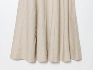 Detailed close-up of panelled hemline on a beige linen midi dress with natural texture