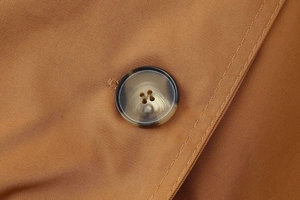 Detail of dark camel twill fabric with amber resin button on double-breasted coat
