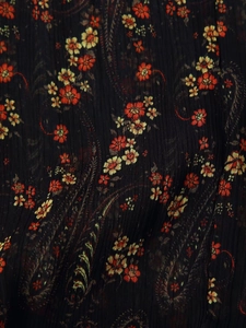 Detailed macro view of black floral chiffon fabric with orange paisley print texture