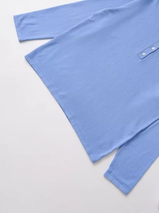 Detail of light blue knit sweater featuring round neck and white buttons on flat lay