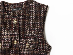 Detail of tweed vest fabric with gold embossed buttons and symmetrical flap pockets