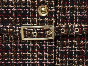 Detailed close-up of textured tweed fabric with metallic gold buckle and button details