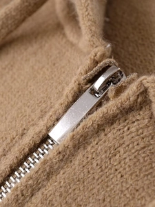 Close-up of silver metal zipper detail on brown knit sweater with textured fabric
