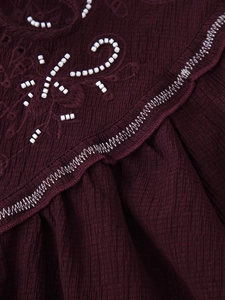 Close-up of wine red woven shirt with floral embroidery and delicate white beadwork