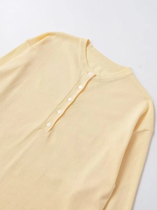 Close-up of a pale yellow long-sleeve knit top featuring a round neck with five white buttons