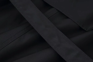 Detail of parallel double-needle stitching on black twill fabric of a short trench coat