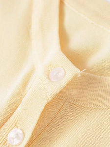 Close-up of knit fabric texture and translucent pearlescent buttons on a yellow cardigan