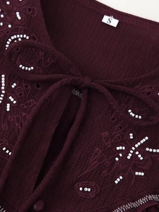 Detail of beaded flower embroidery and ribbed texture on burgundy top neckline