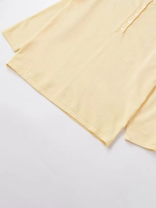 Detailed close-up of the light yellow knit sweater featuring buttoned round neckline