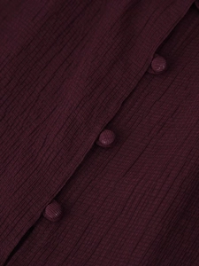 Close-up of deep burgundy pleated fabric with matching fabric-covered buttons on blouse