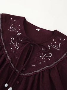 Detail of beaded embroidery on the collar of a wine red shirt with a tie-neck design