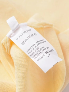 Detailed view of the 100% polyester knit fabric texture and care label on the yellow sweater