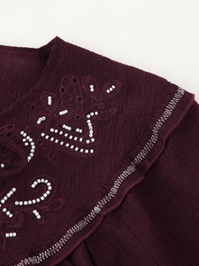 Close-up of burgundy beaded embroidery and ribbed fabric detail on a women shirt