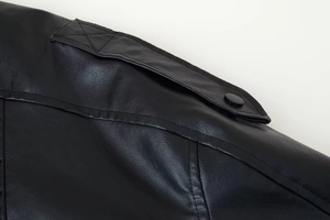 Détail de l'épaule d'une veste en cuir noir montrant la texture et le bouton-pression mat