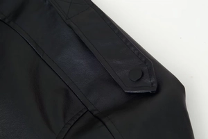 Gros plan de la veste en cuir noir montrant la texture fine et le détail du bouton rond