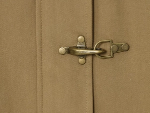 Detailed macro view of bronze metal hook clasp on khaki canvas utility jacket
