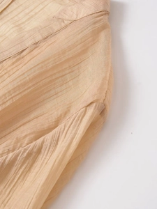 Detail of light brown pleated fabric showing vertical texture and delicate sewing seams