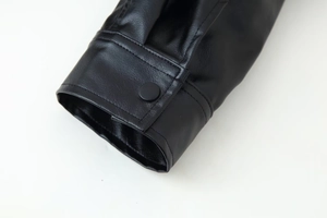 Détail du poignet d'une veste en simili cuir noir avec bouton pression mat et doubles coutures