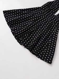 Detail of V-neck dress featuring pleated black fabric with classic white polka dots