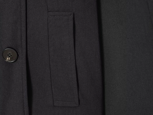 Detailed macro view of a black wool coat featuring a square flap pocket and textured button