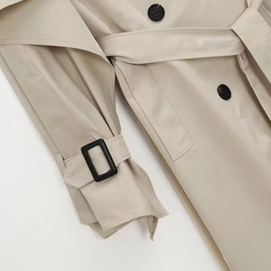 Detail of light beige trench coat sleeve strap and belt with black buckle hardware