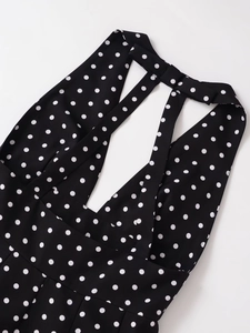 Detail of V-neck halter dress featuring classic white polka dots on a smooth black fabric