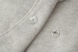Close-up of silver metal snap buttons and high-quality grey wool fabric texture
