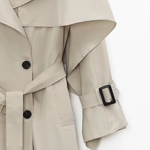 Detail of a beige trench coat featuring classic large black buttons and a waist belt