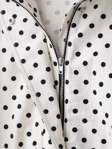 Detailed close-up of white polka dot jacket with silver metal zipper and snap button