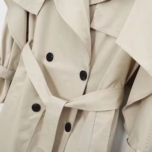 Detail of double-breasted trench coat with black buttons and matching waist belt
