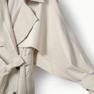 Detail of light beige trench coat featuring classic lapels and high-density woven fabric