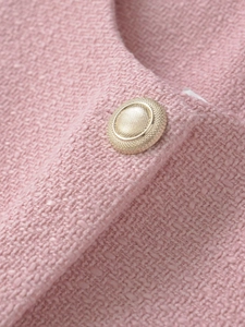Detail of pink tweed fabric texture and a decorative gold button on an elegant vest