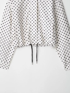 Detailed view of white polka dot jacket featuring adjustable black drawstring hem