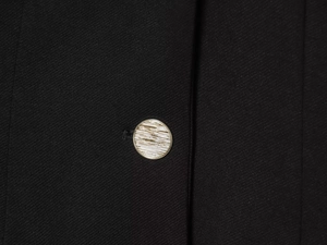 Détail du tissu d'un blazer noir avec un bouton en métal doré brossé de haute qualité