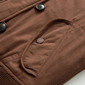 Detail of brown canvas jacket showing tortoiseshell buttons, flap pockets and ribbed hem
