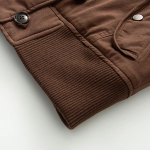 Detailed macro view of the brown canvas jacket cuff with rib knit trim and amber button