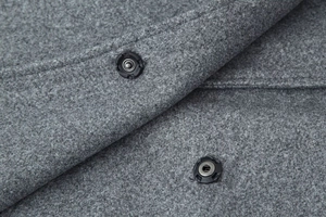 Detail of grey wool-like fabric texture and two black round snap buttons on the jacket