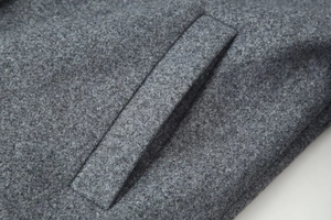 Macro detail of the premium grey wool blend fabric and stitched pocket on the short jacket