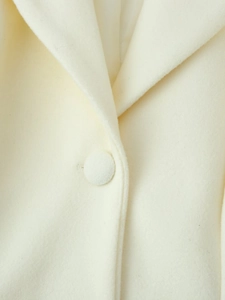 Detail of cream wool coat collar with a matching fabric-covered button and soft texture