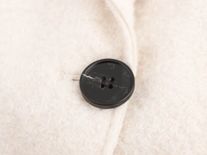 Detail view of a black button on white bouclé wool fabric for this stylish loose coat