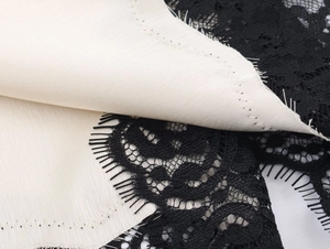 Detail of delicate black eyelash lace stitched on cream satin fabric for a chic look