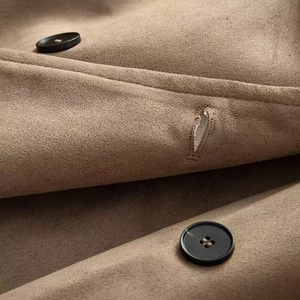 Dettaglio della trama in pelle scamosciata e bottoni neri su un trench color kaki