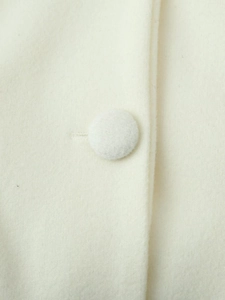 Macro shot of cream wool coat fabric featuring a round fabric-covered button and stitched eyelet