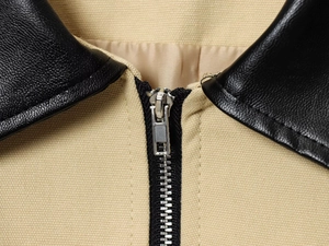 Détail de veste en toile kaki avec col en cuir noir et fermeture éclair en métal argenté