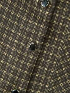 Detail of dark olive plaid fabric with polished black buttons and silver metal trim