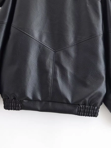 Detail view of black faux leather jacket showing lychee grain texture and hem stitching