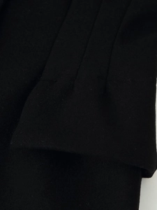 Close-up of black wool coat showing detailed triple parallel stitched pleats on the cuff