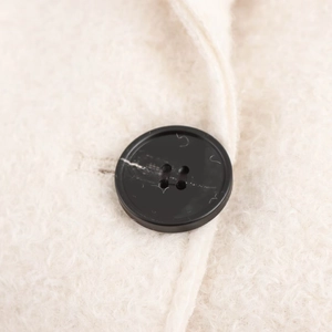 Minimalist beige boucle coat with a matte black four-hole button and fuzzy wool texture
